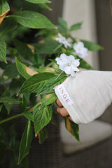 Close-up of the Sheer Wrap Top sleeve and INGE label among white flowers